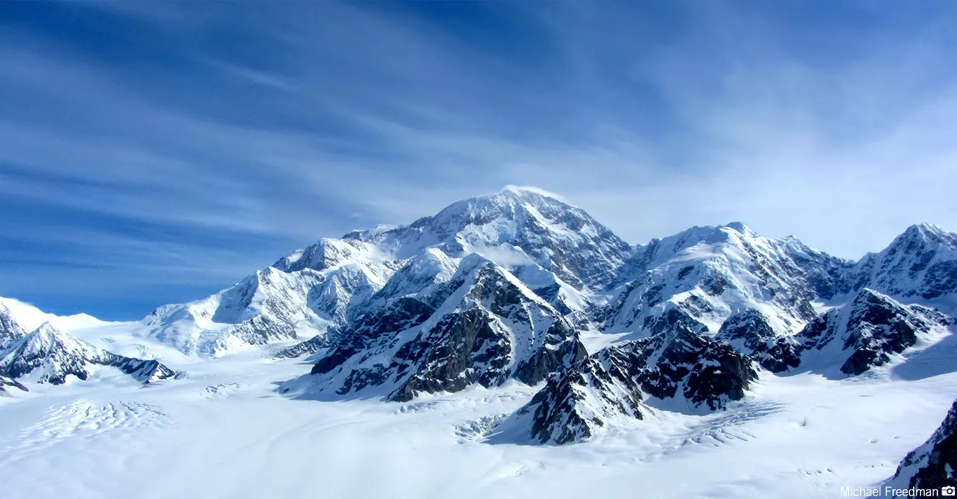 Snow-covered mountain peaks under a partly cloudy blue sky.