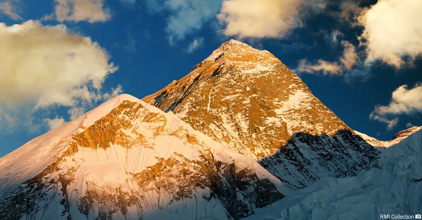 Sunlit snow-covered mountain peaks under a partly cloudy blue sky.