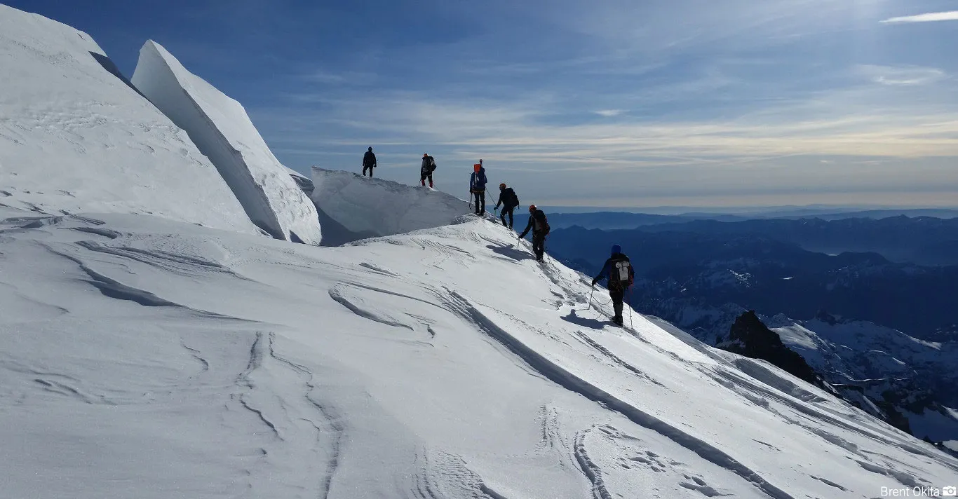 Group of climbers hiking in a line on a snow-covered mountain ridge under a clear sky.