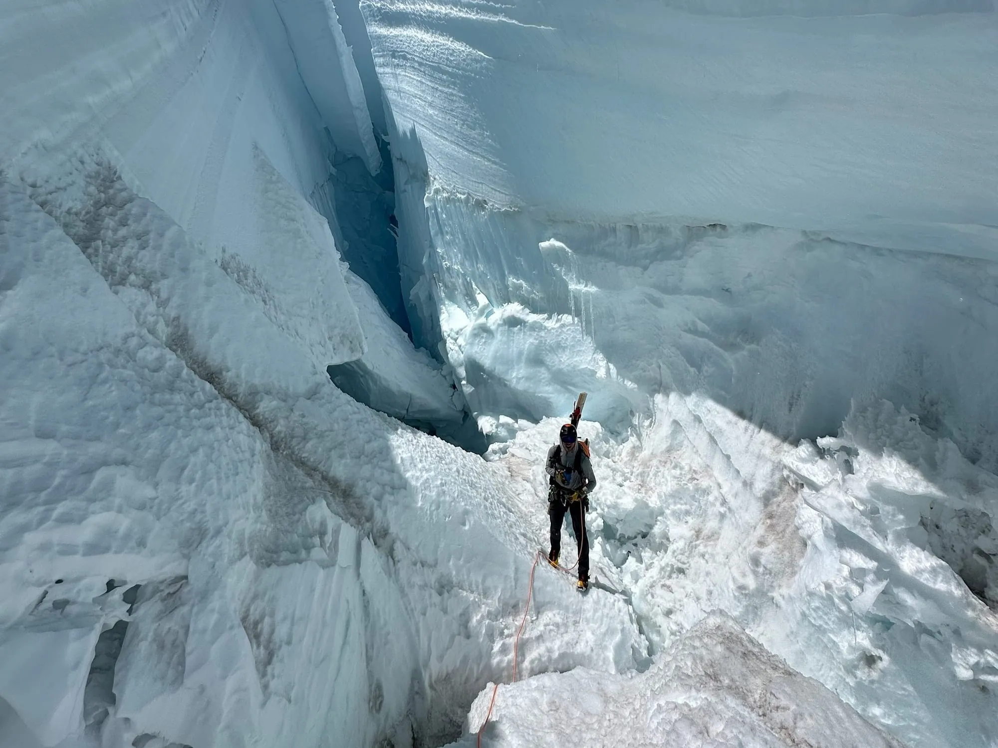 Climber roped in standing on ice inside a deep glacial crevasse with steep icy walls.