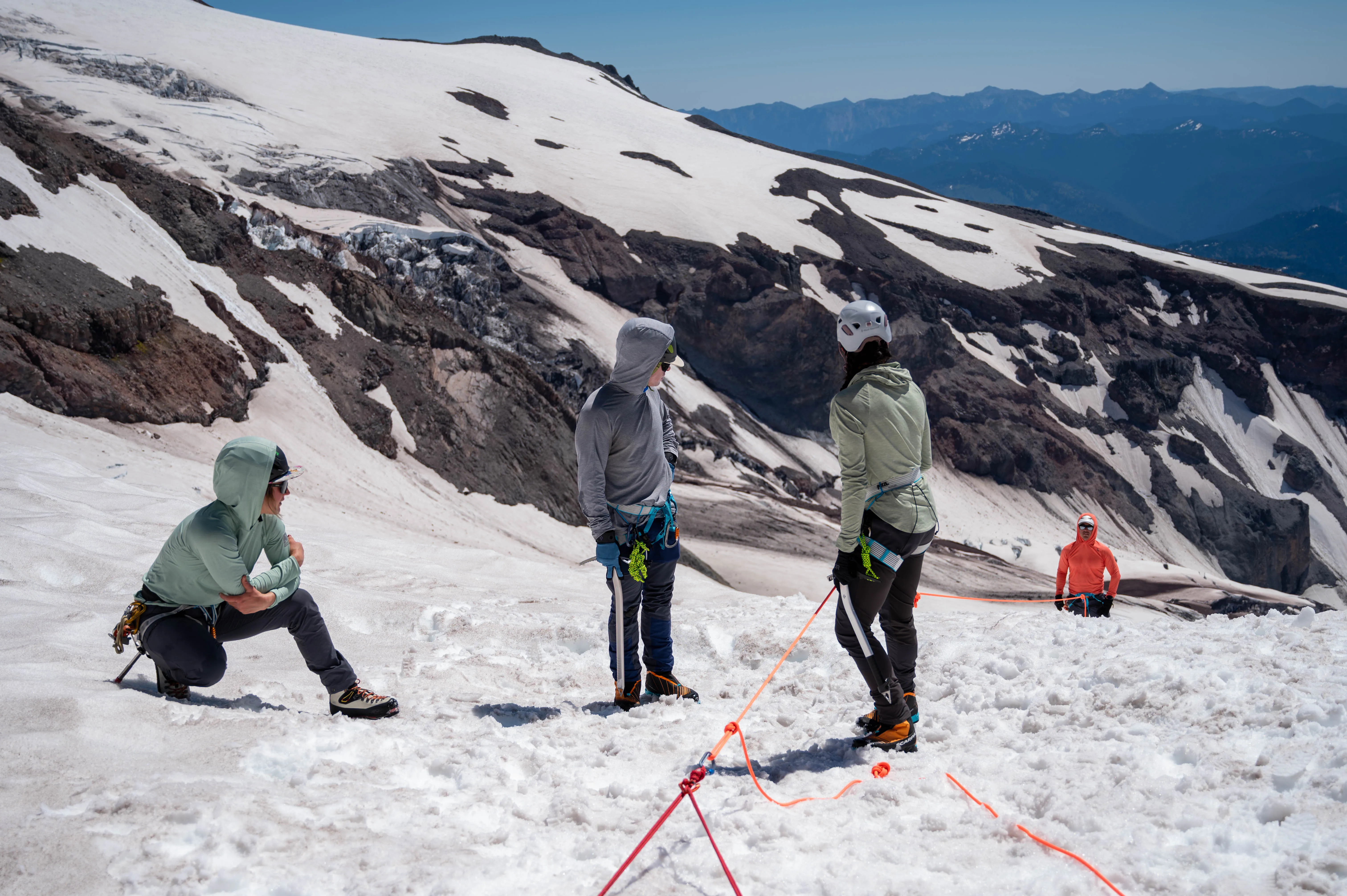 Four climbers with ice axes on snowy mountain slope practicing rope safety techniques.