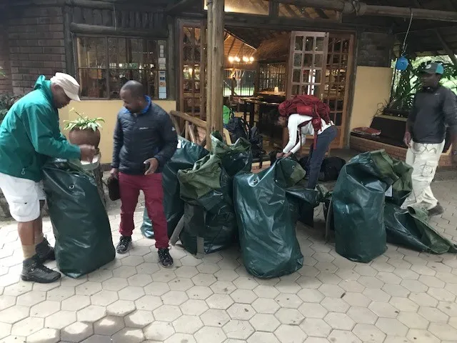 Four people packing and arranging large green bags outside a rustic building with wooden beams.