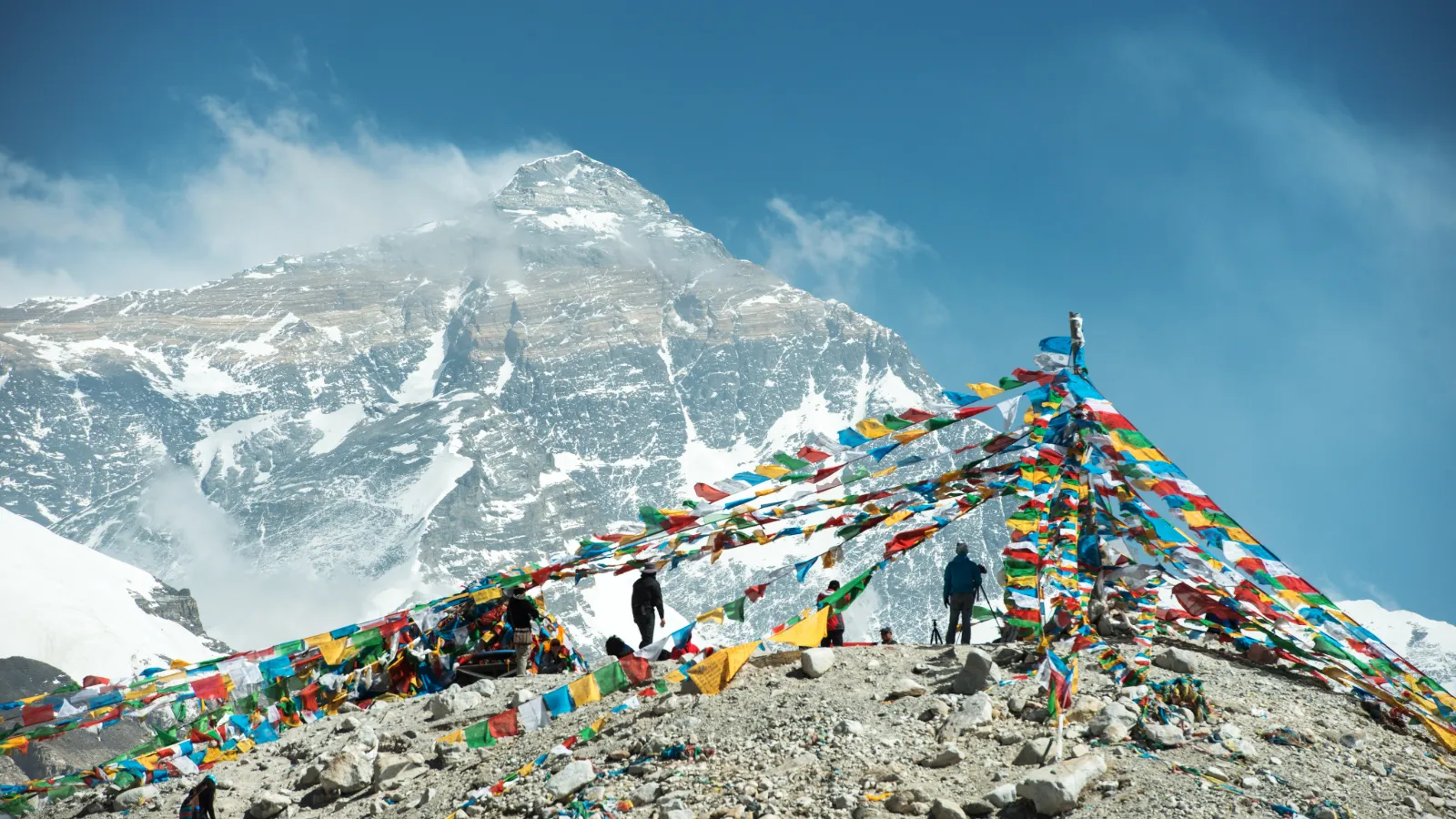 Colorful prayer flags on rocky ground with Mount Everest's snow-covered peak in the background.