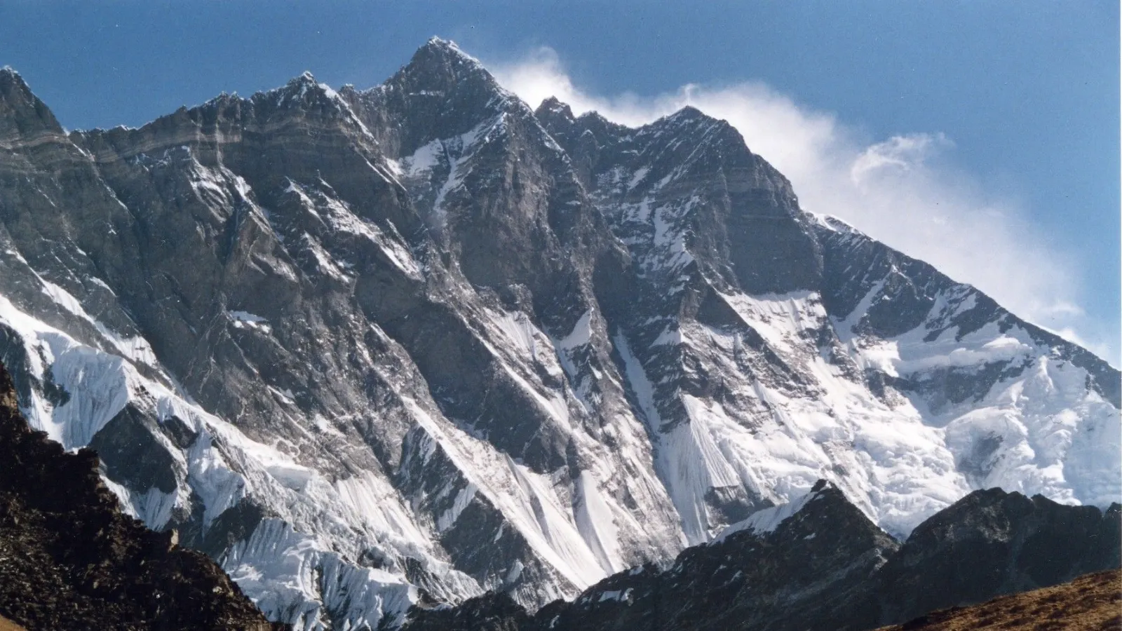 Snow-covered rugged mountain peaks under a clear blue sky with dark rocky foreground ridges.