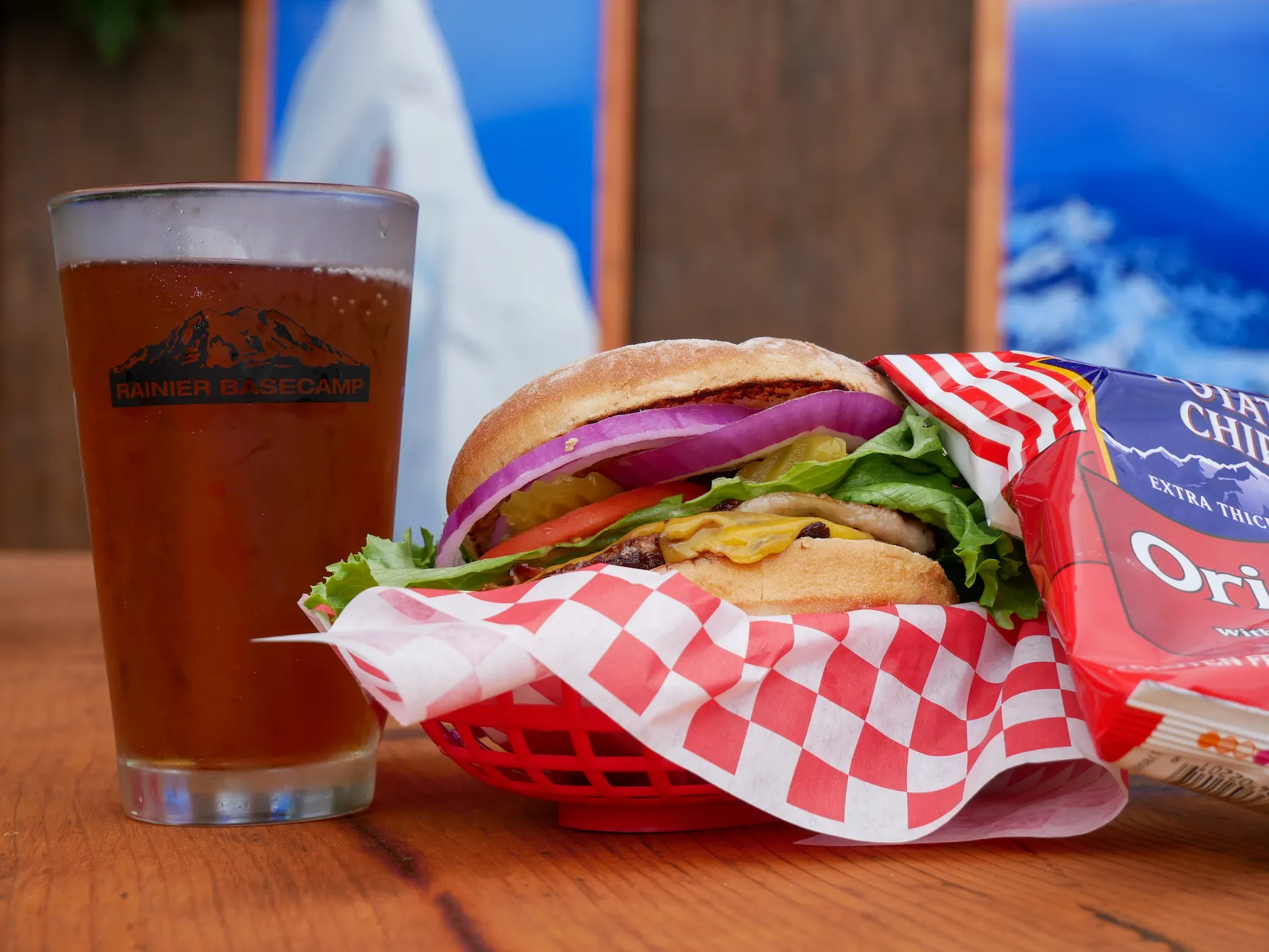 Cheeseburger with lettuce, tomato, onion, and pickles in a basket with chips and a beer glass.